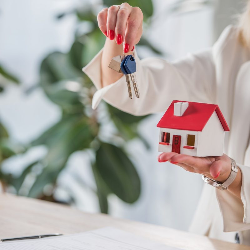partial view of businesswoman showing house model and keys near clipboard and calculator
