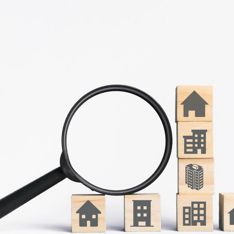 Property icons on wooden cubes with magnifying glass. Concept of property investment analysis.